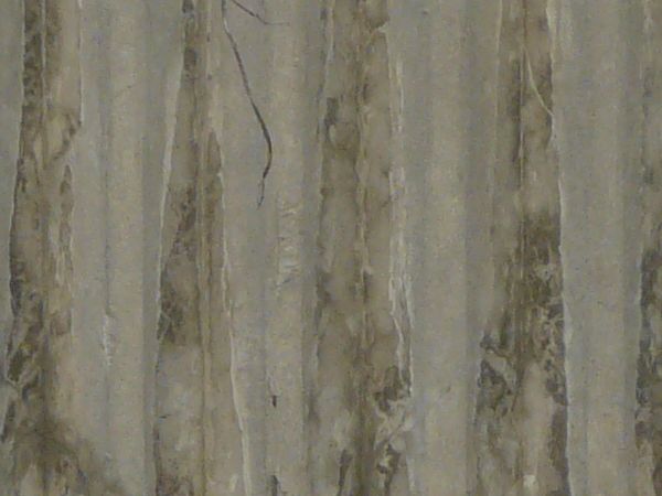 Concrete fence texture molded with a pattern of circles above vertical recessions, with large cracks and stains. The fence appears to be crumbling around the edges.